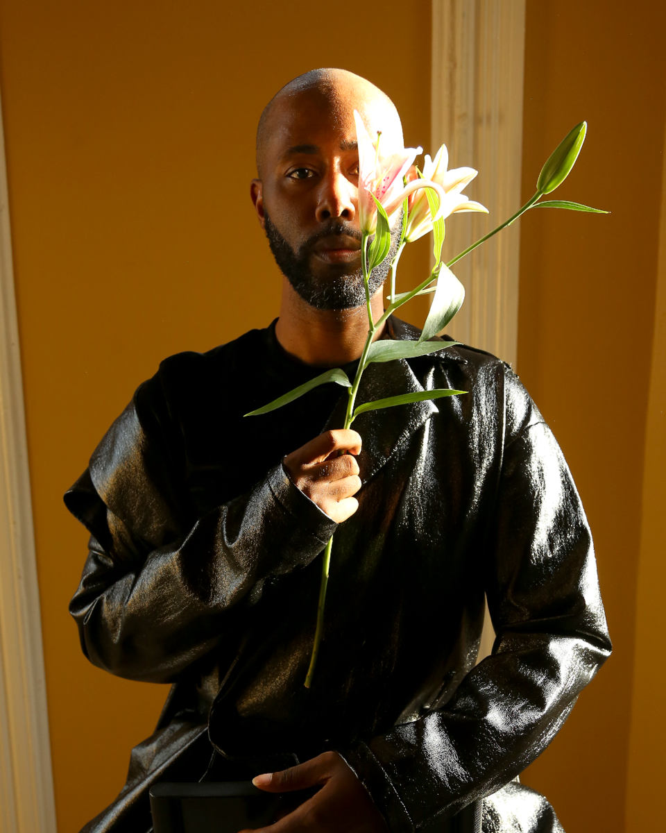 A man with a black beard holds a lily.